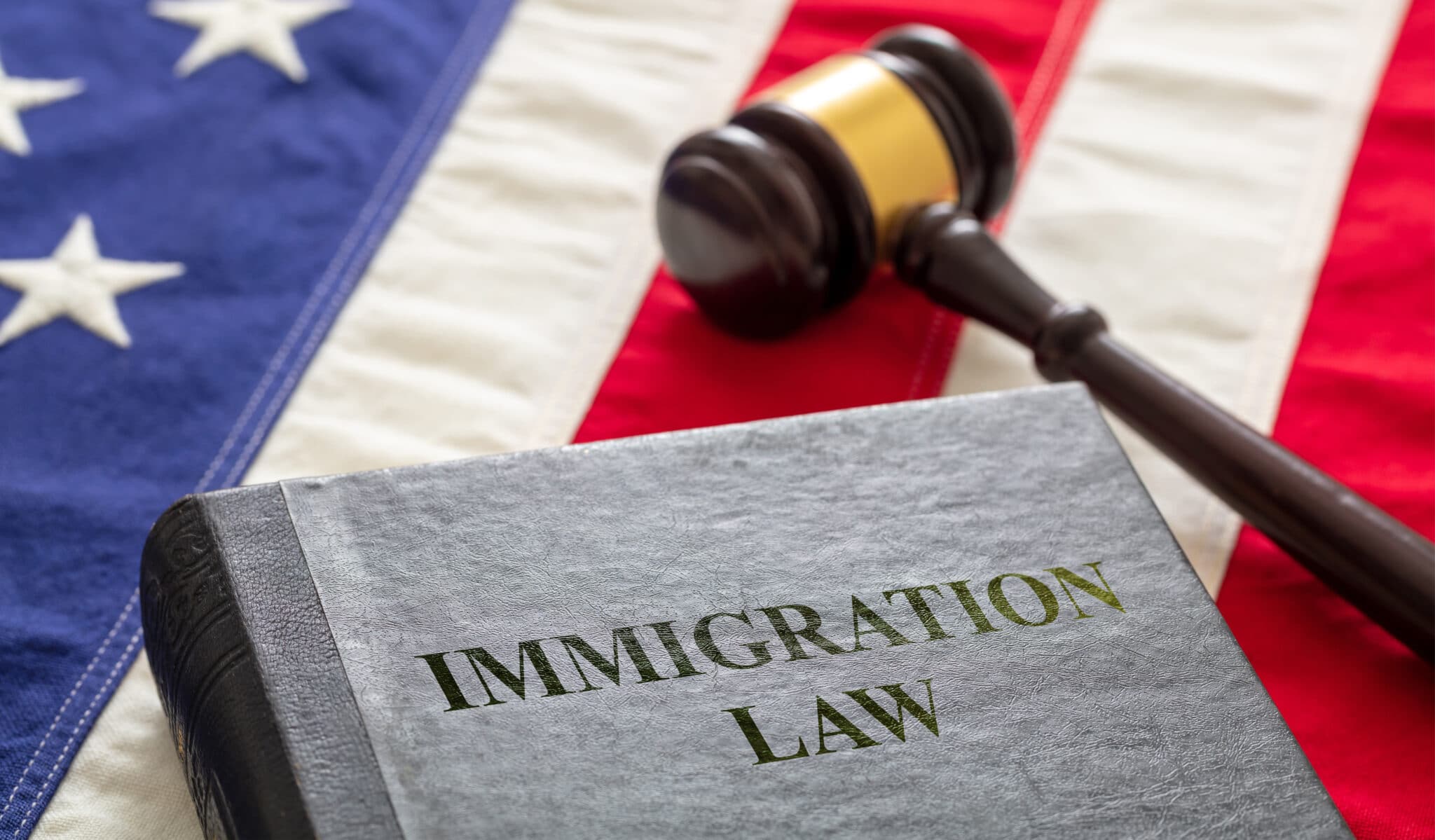 Immigration law text on black book and judge gavel on US of America flag background. Migration, emigration visa in USA concept