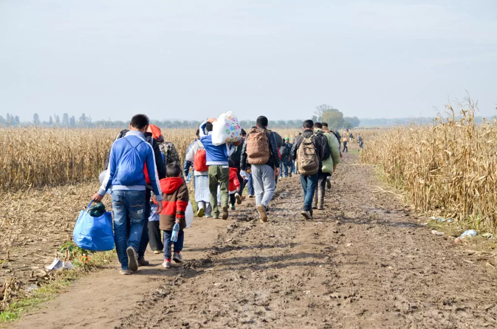 A line of migrants walking along a dirt path in El Paso.