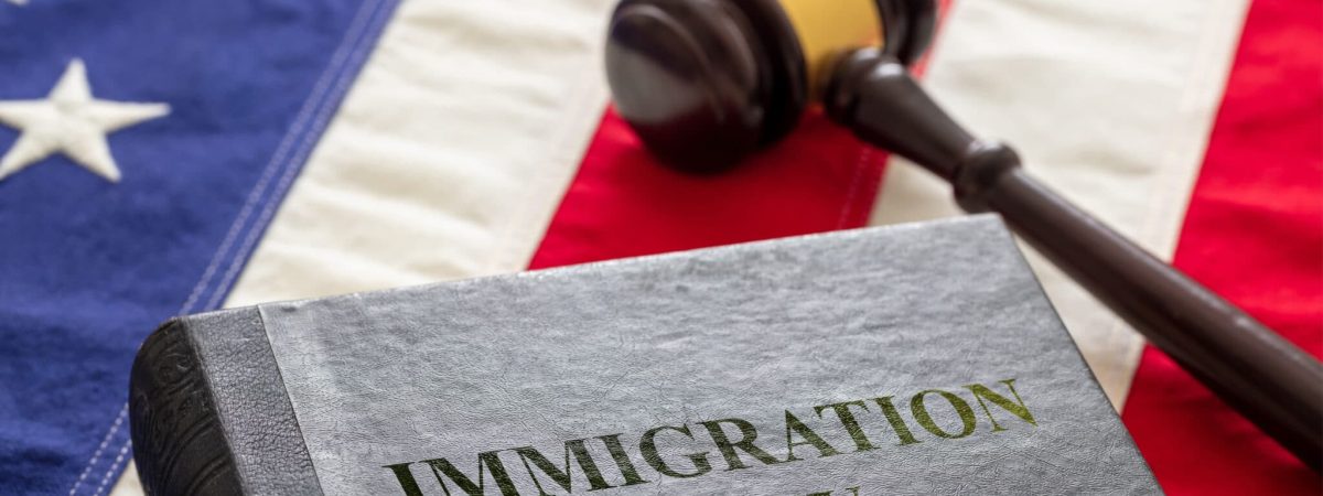 Immigration law text on black book and judge gavel on US of America flag background. Migration, emigration visa in USA concept