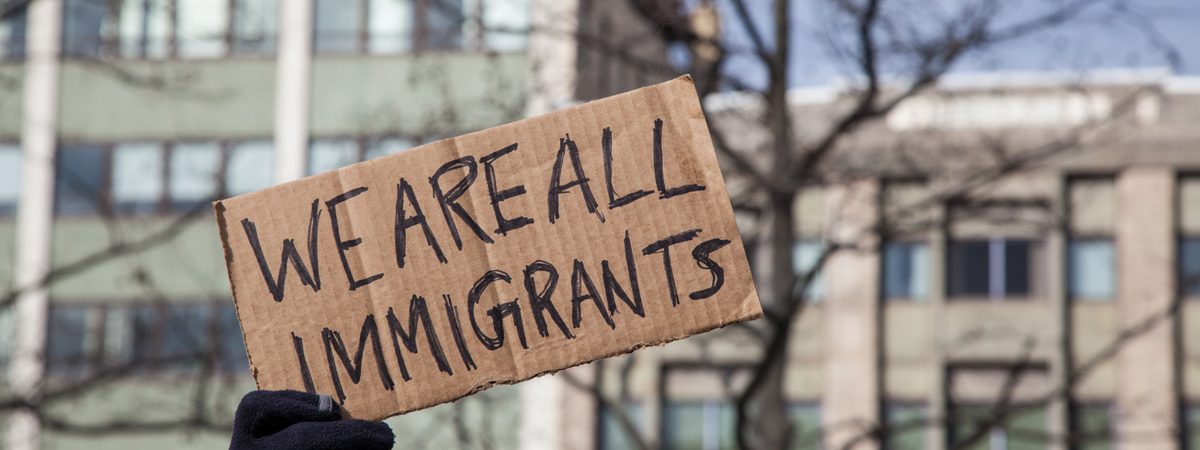 A hand holding up a cardboard sign that reads “WE ARE ALL IMMIGRANTS” in El Paso.