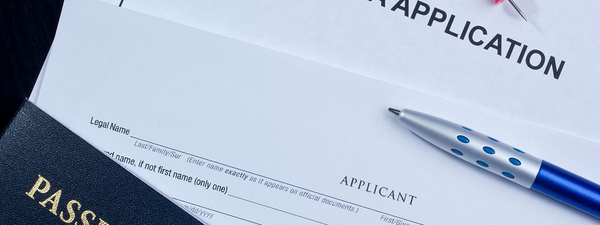 A white piece of paper reading “VISA APPLICATION” next to a blue pen and United States passport in El Paso.