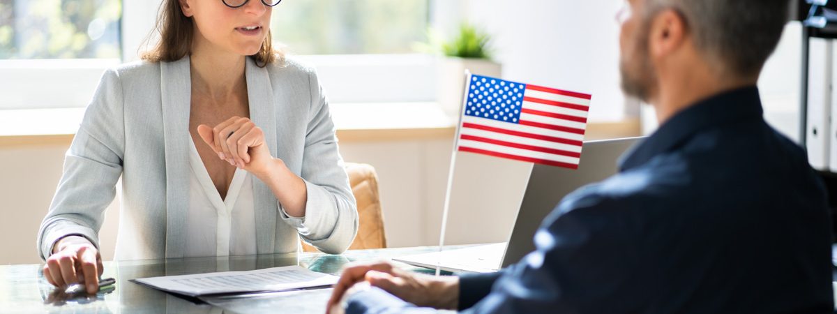 An immigration lawyer and client speaking at a glass desk with an American flag on it in El Paso.