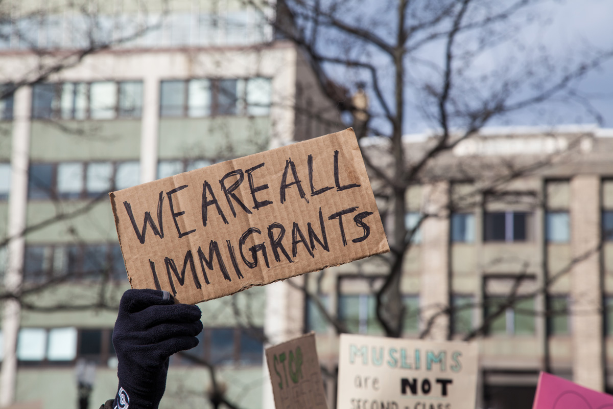 A hand holding up a cardboard sign that reads “WE ARE ALL IMMIGRANTS” in El Paso.