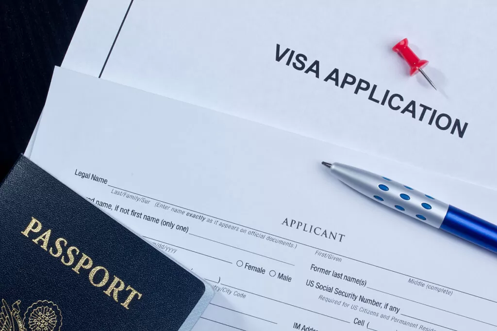 A white piece of paper reading “VISA APPLICATION” next to a blue pen and United States passport in El Paso.