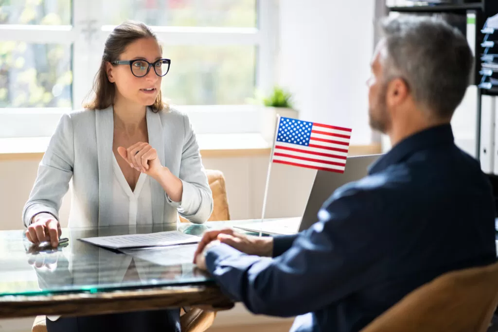 An immigration lawyer and client speaking at a glass desk with an American flag on it in El Paso.
