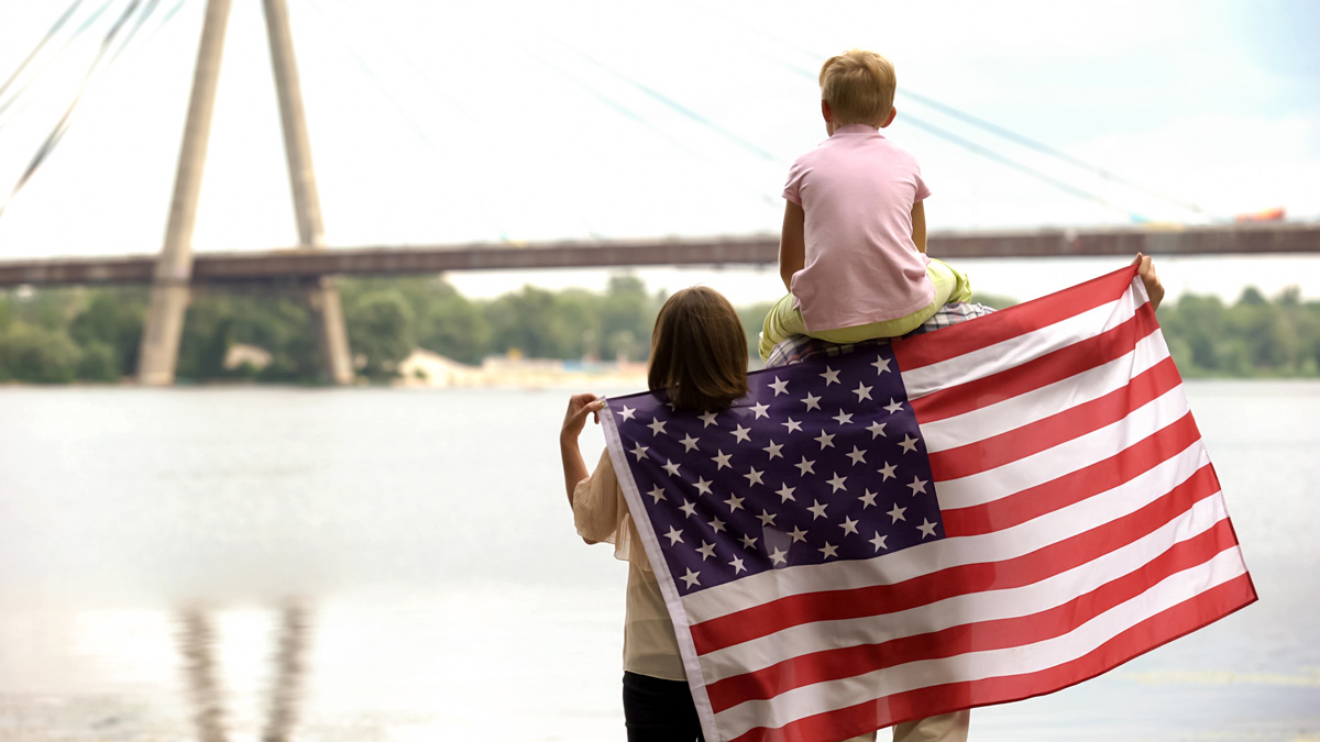 A family standing in front of a river holding an American flag behind their backs in El Paso.